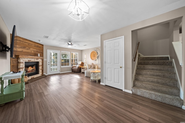 living room with a stone fireplace, visible vents, baseboards, stairway, and dark wood finished floors