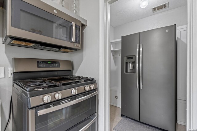 kitchen featuring visible vents, light tile patterned flooring, a textured ceiling, and appliances with stainless steel finishes