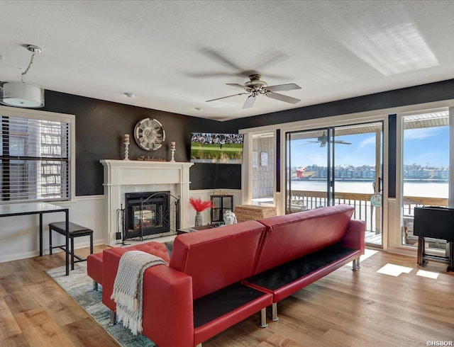 living room with a textured ceiling, wood finished floors, a high end fireplace, and a ceiling fan