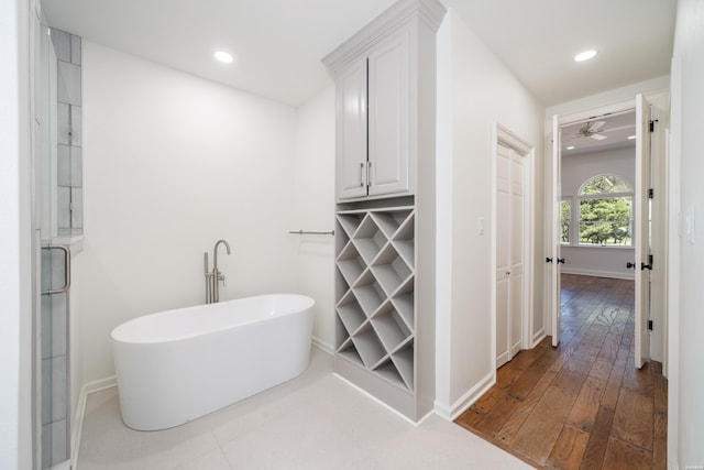 bathroom with a ceiling fan, recessed lighting, a soaking tub, baseboards, and hardwood / wood-style flooring