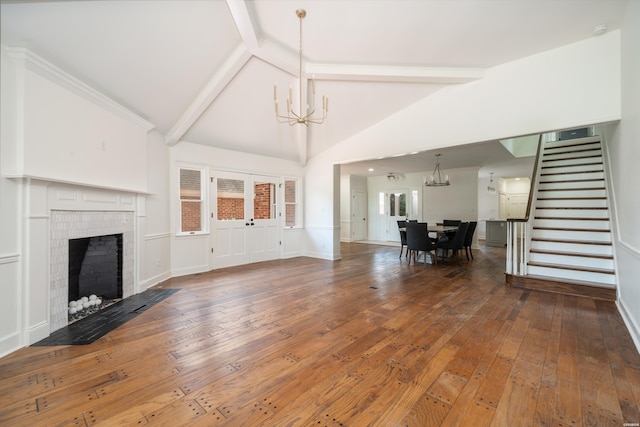 unfurnished living room with hardwood / wood-style flooring, stairway, a chandelier, a brick fireplace, and beamed ceiling