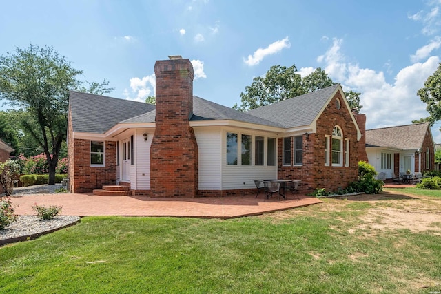 back of house featuring a yard, brick siding, a patio, and a chimney