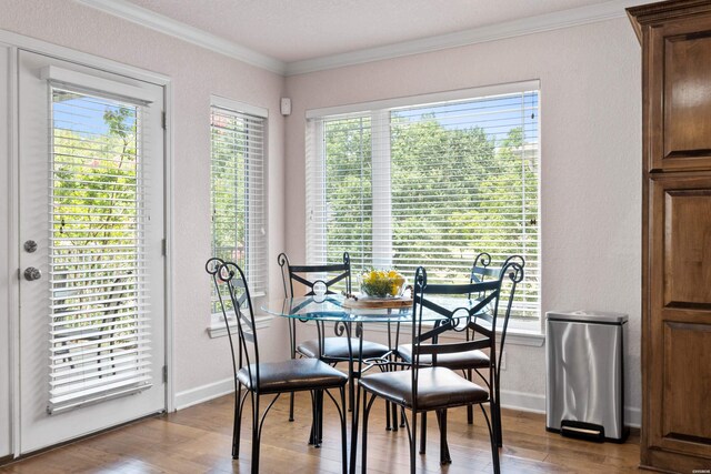 dining room featuring a textured wall, ornamental molding, wood finished floors, and baseboards