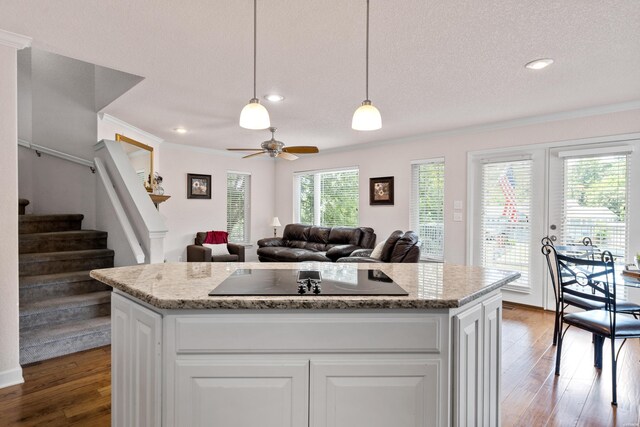 kitchen featuring white cabinets, wood finished floors, a center island, hanging light fixtures, and black electric stovetop