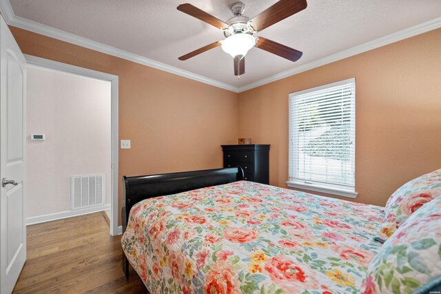 bedroom featuring ornamental molding, visible vents, ceiling fan, and wood finished floors