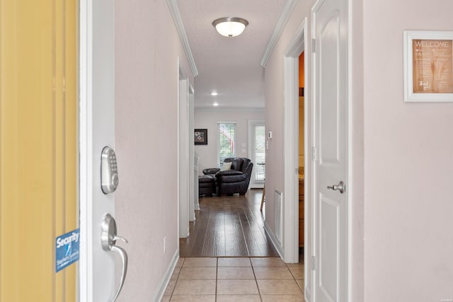 corridor featuring light tile patterned flooring, crown molding, visible vents, and baseboards