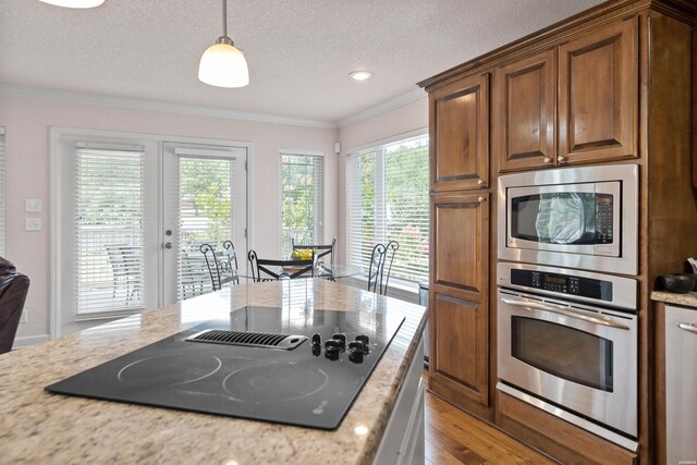 kitchen with decorative light fixtures, light stone countertops, stainless steel appliances, crown molding, and light wood-style floors