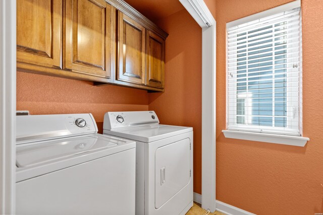 clothes washing area featuring washing machine and dryer, cabinet space, a textured wall, and baseboards