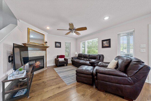 living room with a textured ceiling, a tile fireplace, wood finished floors, baseboards, and crown molding