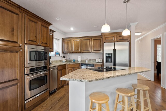 kitchen with a center island, pendant lighting, stainless steel appliances, light stone countertops, and a kitchen bar