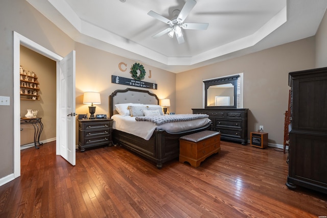 bedroom with a ceiling fan, baseboards, a raised ceiling, and dark wood-style flooring