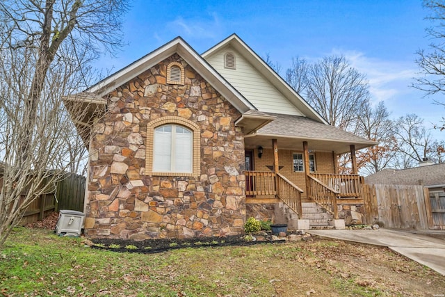 view of front facade with a porch, brick siding, a shingled roof, and fence