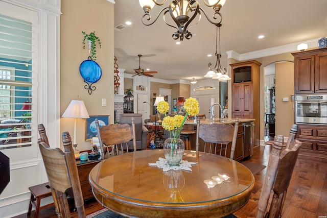 dining space featuring crown molding, ceiling fan with notable chandelier, arched walkways, and dark wood-style flooring