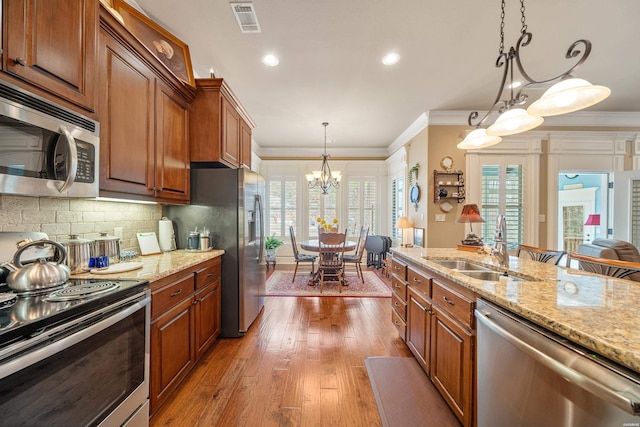 kitchen featuring visible vents, a sink, appliances with stainless steel finishes, an inviting chandelier, and brown cabinetry