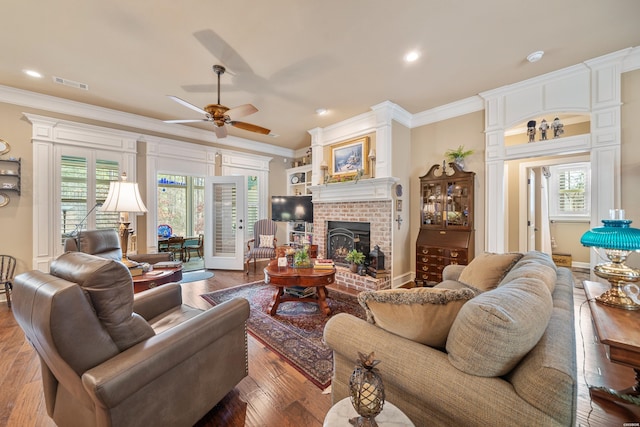 living room with hardwood / wood-style floors, visible vents, a fireplace, ceiling fan, and crown molding