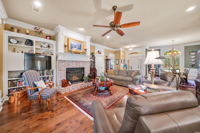 living room featuring visible vents, a brick fireplace, ornamental molding, ceiling fan with notable chandelier, and wood finished floors