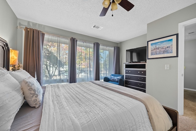 carpeted bedroom featuring a textured ceiling, baseboards, visible vents, and a ceiling fan