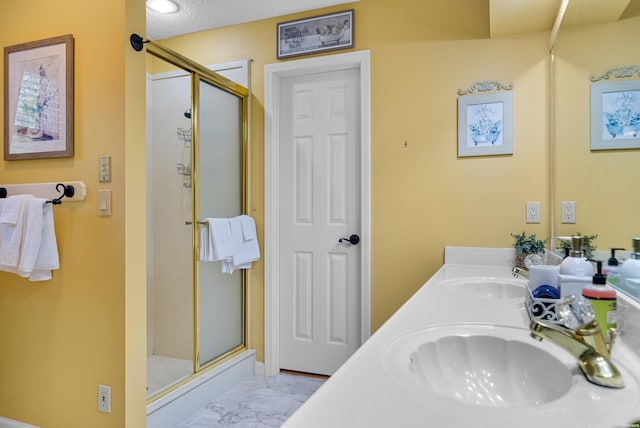 bathroom featuring a sink, a shower stall, a textured ceiling, and double vanity