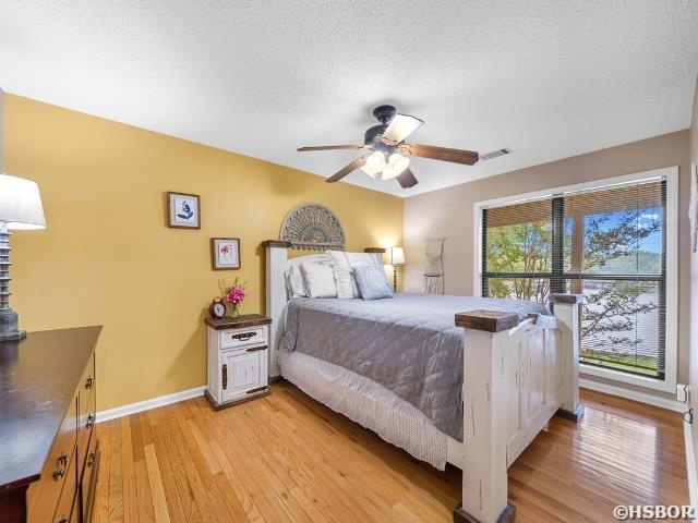 bedroom featuring light wood finished floors, visible vents, a ceiling fan, a textured ceiling, and baseboards