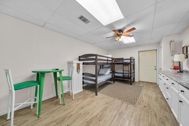 bedroom with visible vents, ceiling fan, light wood-type flooring, a drop ceiling, and baseboards