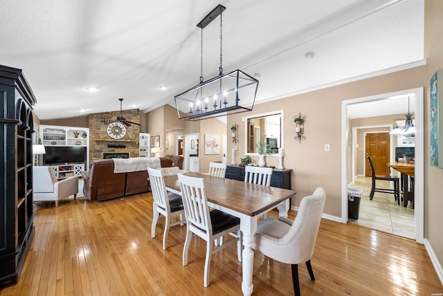 dining space featuring light wood-type flooring, vaulted ceiling, a stone fireplace, and baseboards