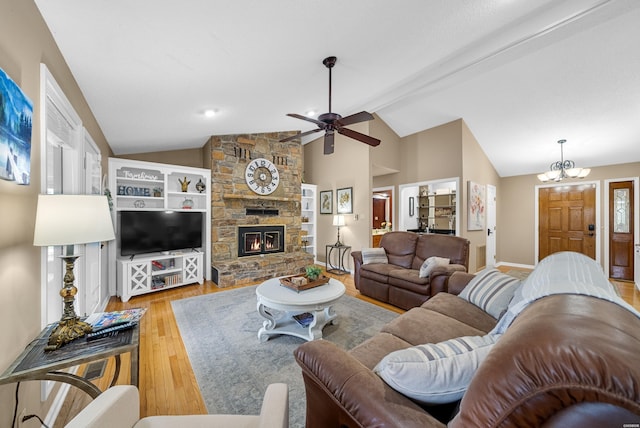 living room with baseboards, vaulted ceiling with beams, light wood-type flooring, a fireplace, and ceiling fan with notable chandelier