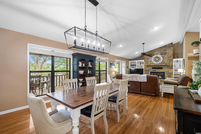 dining space with lofted ceiling, light wood-type flooring, a stone fireplace, and baseboards