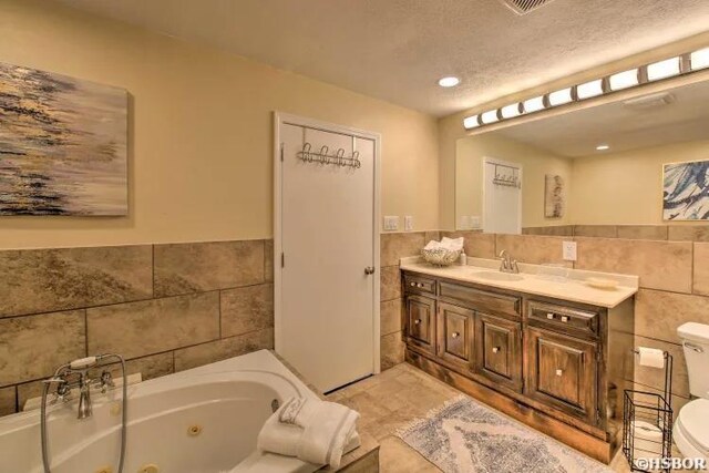 bathroom with tile walls, toilet, wainscoting, vanity, and a whirlpool tub