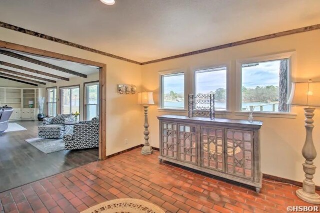 interior space with crown molding, vaulted ceiling with beams, brick floor, and baseboards