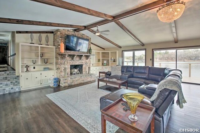 living area featuring lofted ceiling with beams, ceiling fan, stairway, dark wood-style flooring, and a fireplace