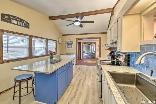 kitchen with blue cabinets, a sink, white cabinets, stainless steel range oven, and decorative backsplash