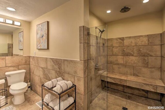 bathroom with toilet, recessed lighting, tile walls, wainscoting, and a shower stall