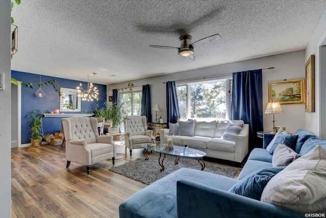 living area featuring ceiling fan with notable chandelier, a textured ceiling, and wood finished floors