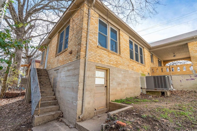 view of side of home featuring stairway, brick siding, and central AC