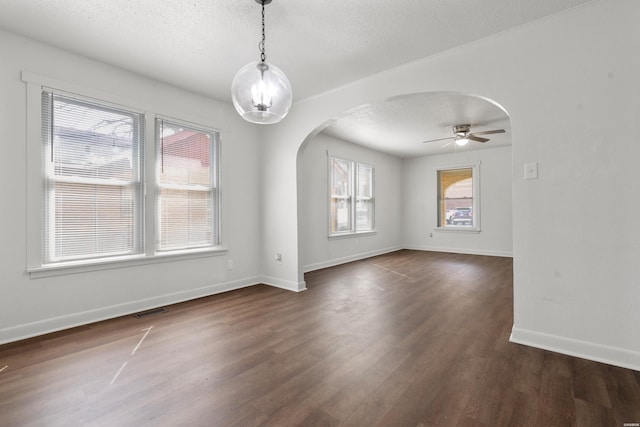 unfurnished room with arched walkways, visible vents, dark wood finished floors, and a textured ceiling