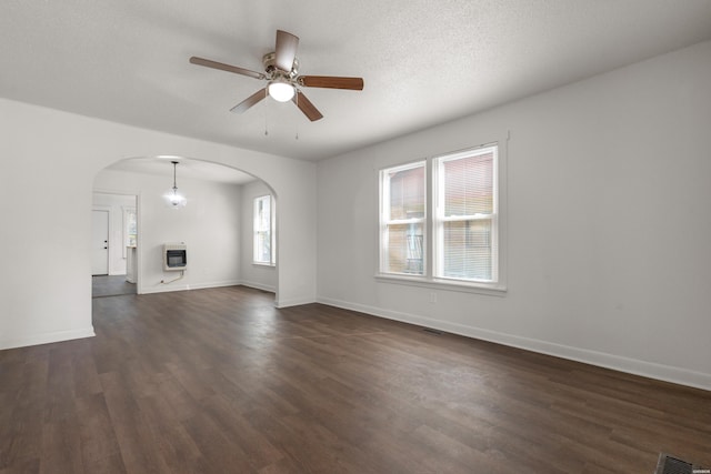 unfurnished living room with dark wood-type flooring, heating unit, a textured ceiling, arched walkways, and baseboards