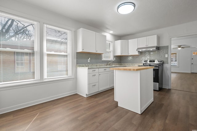 kitchen with dark wood finished floors, stainless steel electric stove, white cabinets, under cabinet range hood, and butcher block counters