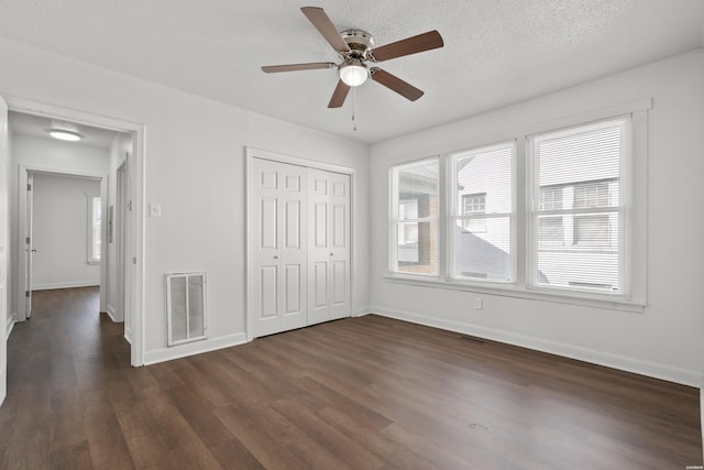 unfurnished bedroom featuring visible vents, baseboards, a textured ceiling, and dark wood-style floors