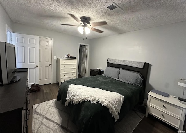 bedroom featuring dark wood-style floors, a textured ceiling, visible vents, and a ceiling fan