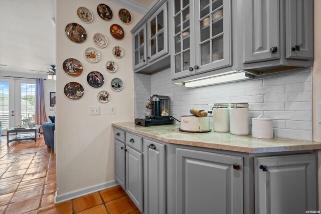 kitchen featuring light countertops, decorative backsplash, glass insert cabinets, and gray cabinetry