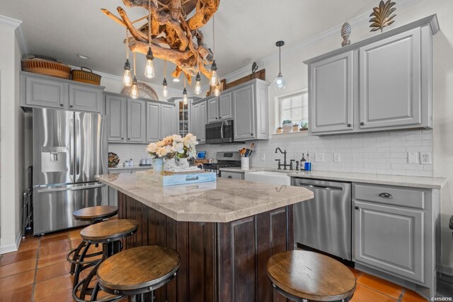 kitchen with stainless steel appliances, a sink, a kitchen island, hanging light fixtures, and light stone countertops