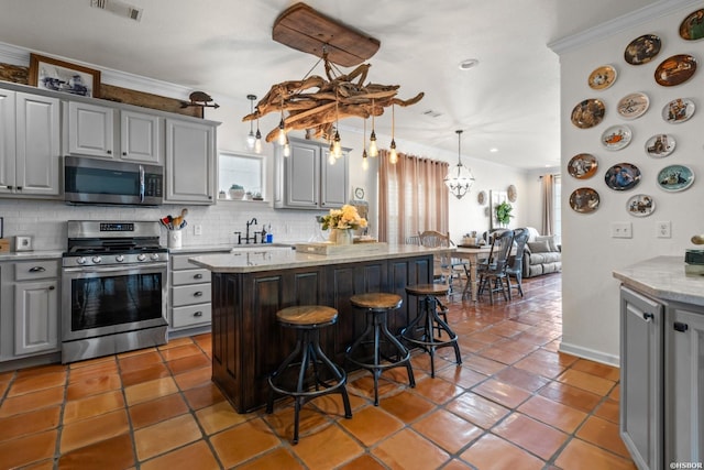 kitchen with visible vents, a kitchen island, a breakfast bar, stainless steel appliances, and gray cabinetry