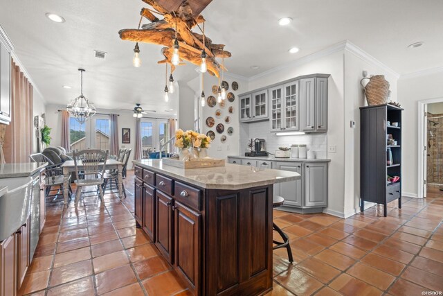 kitchen featuring decorative light fixtures, gray cabinets, backsplash, glass insert cabinets, and a kitchen island