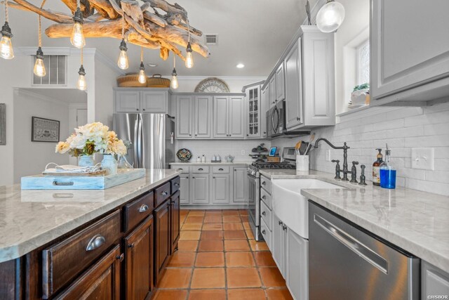 kitchen featuring stainless steel appliances, tasteful backsplash, gray cabinets, glass insert cabinets, and ornamental molding