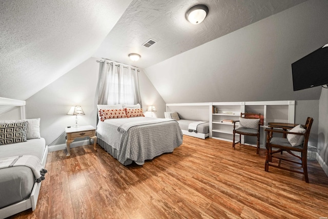 bedroom with wood finished floors, baseboards, visible vents, lofted ceiling, and a textured ceiling