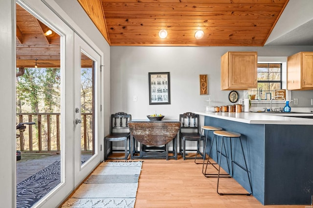 kitchen with light countertops, vaulted ceiling, a kitchen bar, wooden ceiling, and light wood-type flooring