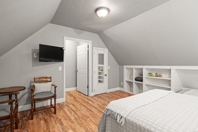 bedroom with baseboards, a textured ceiling, wood finished floors, and vaulted ceiling