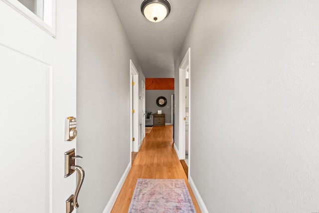 corridor featuring light wood-type flooring and baseboards