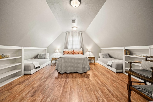 bedroom with visible vents, a textured ceiling, wood finished floors, and vaulted ceiling