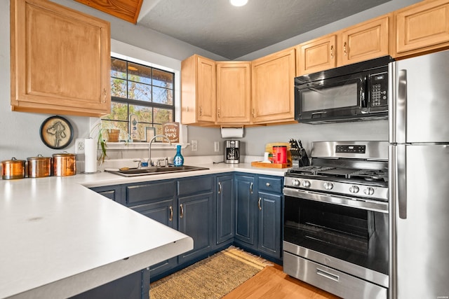 kitchen with light brown cabinets, blue cabinetry, a sink, stainless steel appliances, and light countertops